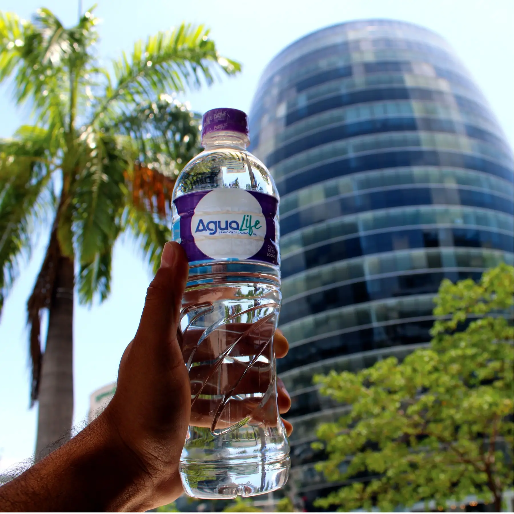 Mano sosteniendo una botella Agualife frente a un edificio de Guayaquil